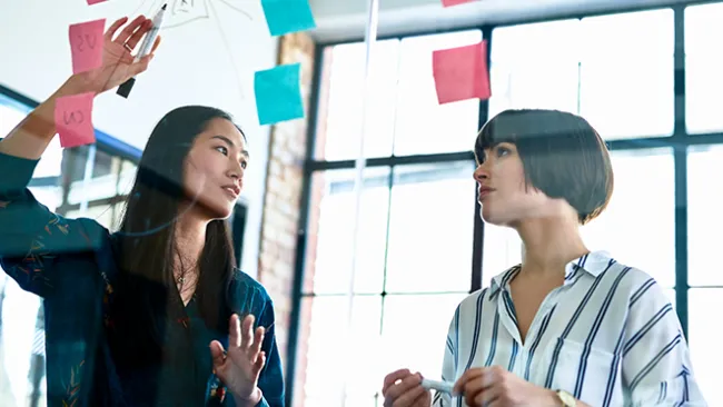 Two women looking at post-it notes on a board