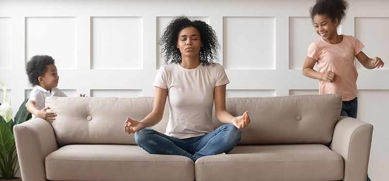 Mother in a yoga pose on a couch surrounded by her children