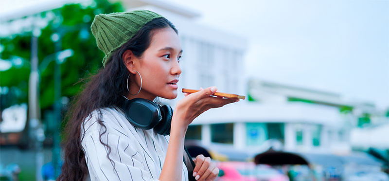 Woman wearing headphones around her neck and talking into a smartphone